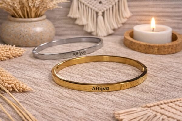 Ατσάλινη χειροπέδα σε χρυσή απόχρωση, χαραγμένη με το όνομα ΑΘΗΝΑ.